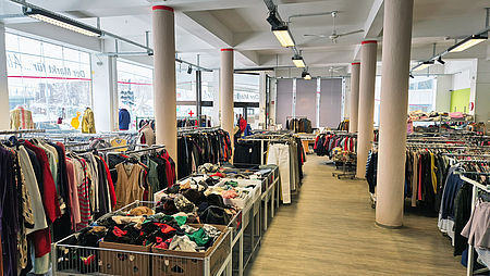 Ein Foto vom Geschäftsraum unseres Markt für Alle. Zu sehen sind viele Garderobenstangen und Wühlfächer mit diversen Kleidungen.