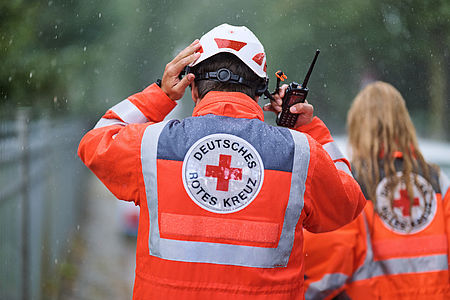 Zwei Einsatzkräfte in Einsatzkleidung, eine Person setzt sich einen Schutzhelm auf und hält dabei das Funkgerät an sein Ohr.